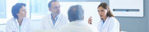 Four scientists are sitting around a table in lab coats in a meeting