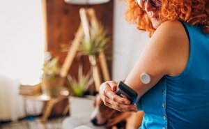 An image of a woman wearing a continuous glucose monitor, using her smartphone to view the data