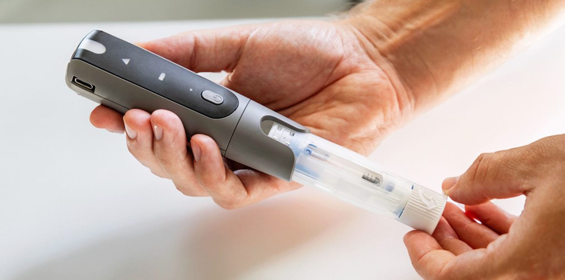 An image of the Phillips Medisize Aria Smart Autoinjector in a male's hands. He is inserting the cartridge into the reusable device.