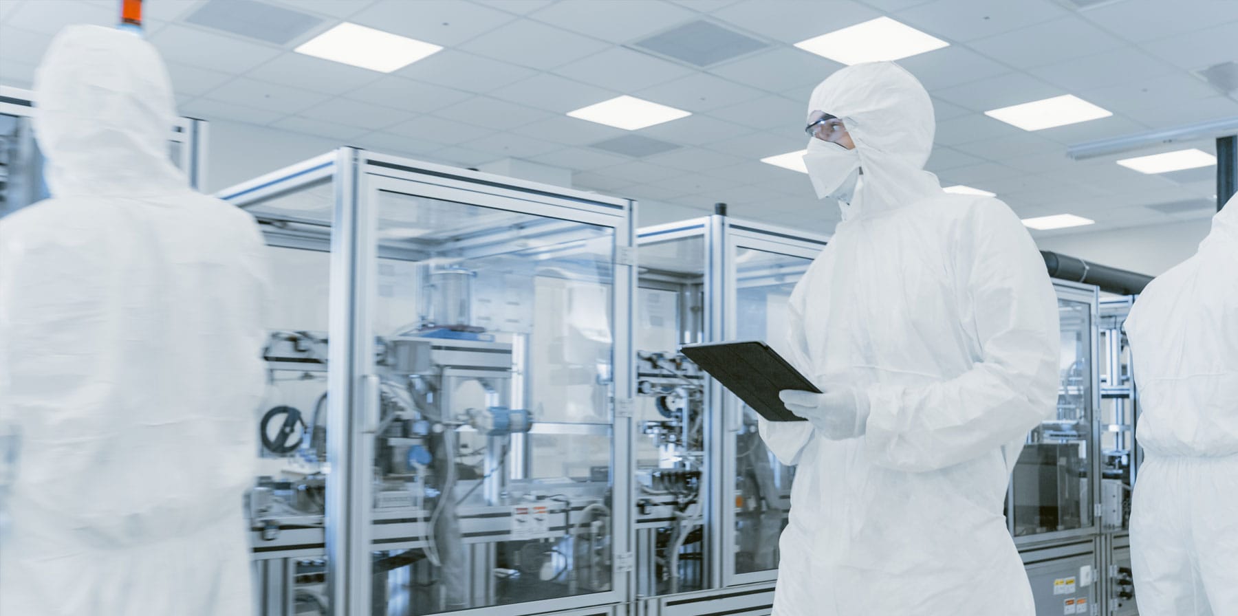 Two scientists walking in a manufacturing plant in sterile coveralls and face masks demonstrating CDMO quality and regulatory services using laptop computer.