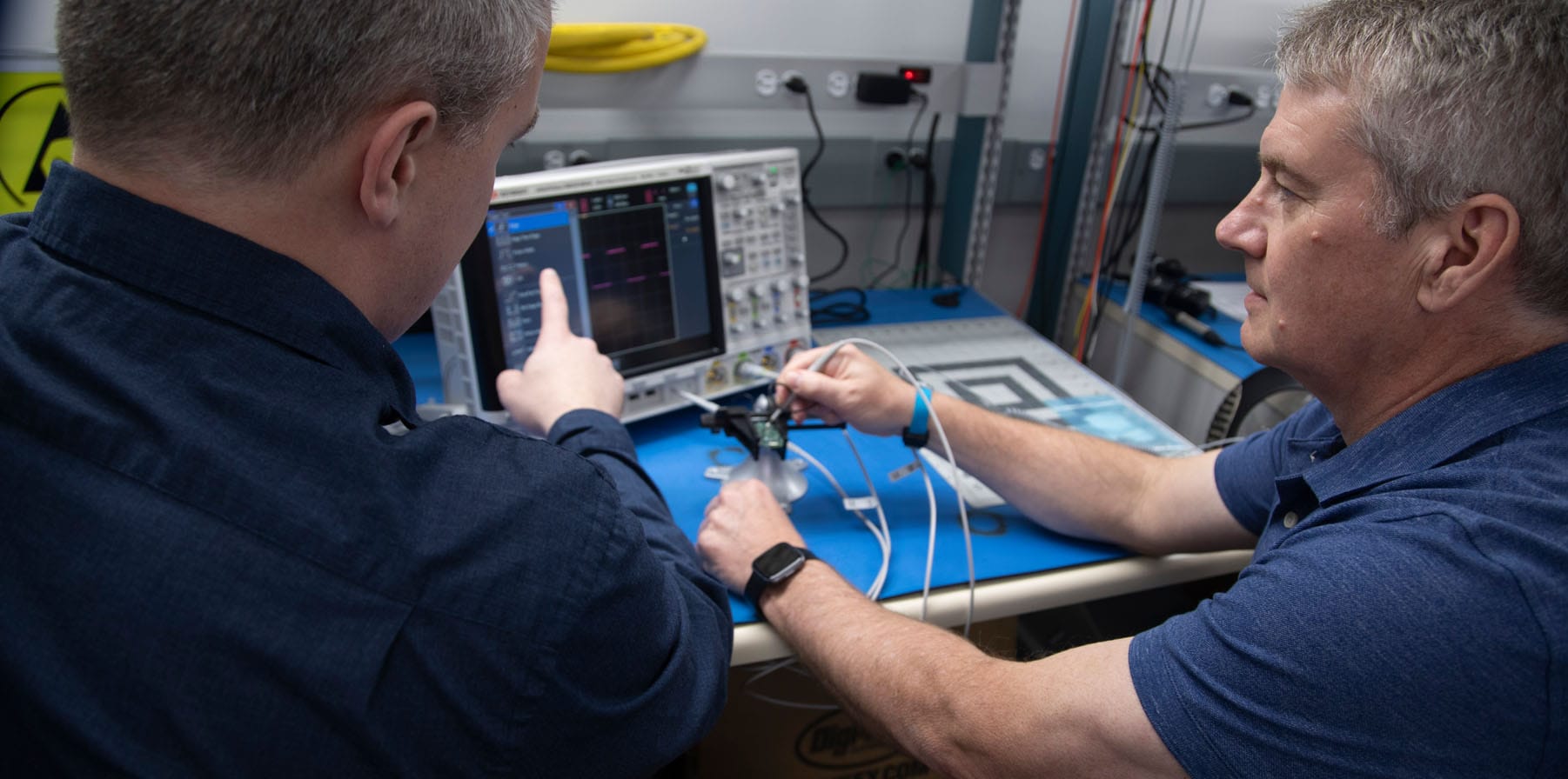 A close-up image of two Phillips Medisize employees looking at a machine while sitting at a desk, discussing their engineering expertise while they work together