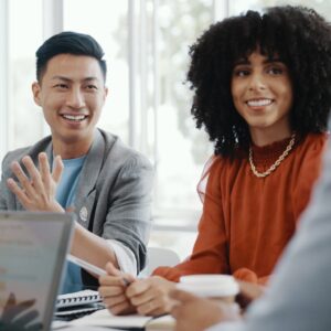 An image of a team meeting in a well-lit room, talking around a table ahead of a customer meeting.