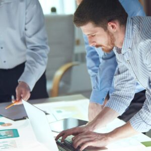 An image of a team working around a table looking at a variety of graphs discussing in front of a laptop.