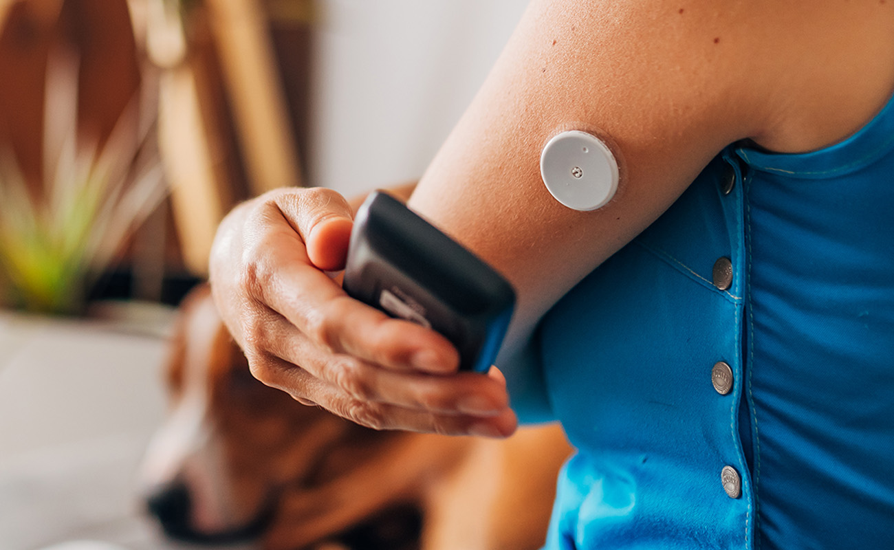 An image of a woman wearing a continuous glucose monitor, using her smartphone to view the data