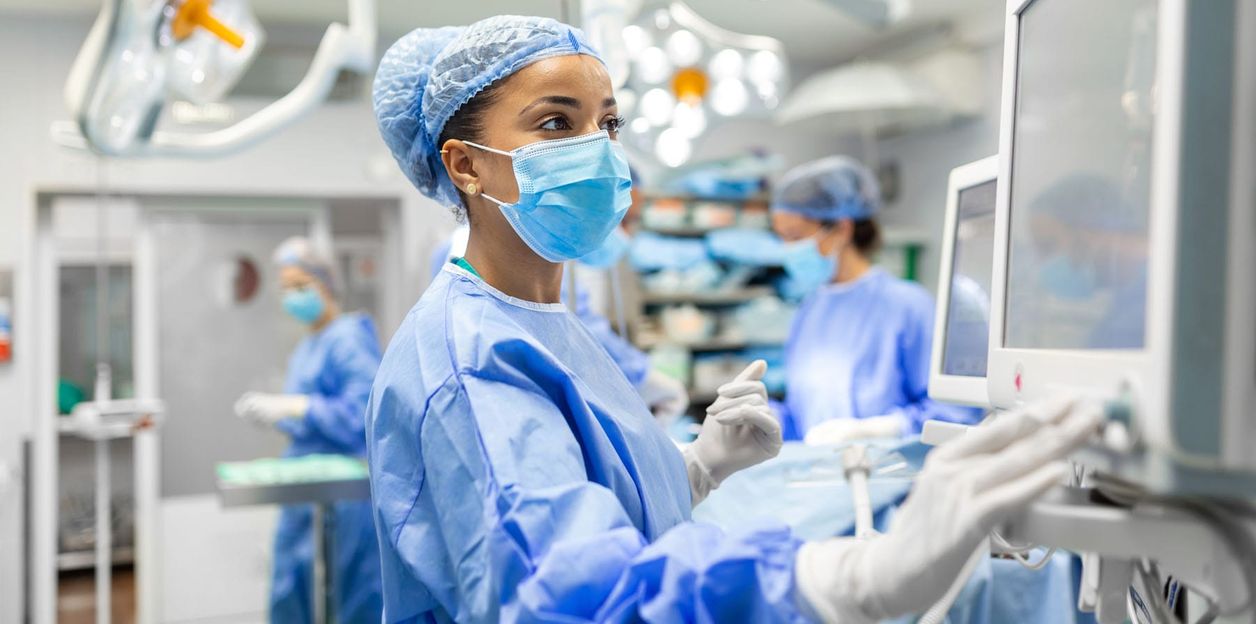 Anesthetist wearing protecive gear checking monitors while sedating patient before a medtech surgical procedure in hospital
