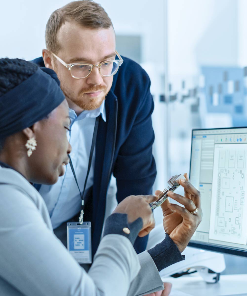 man and woman looking at computer circuit board in front of computer