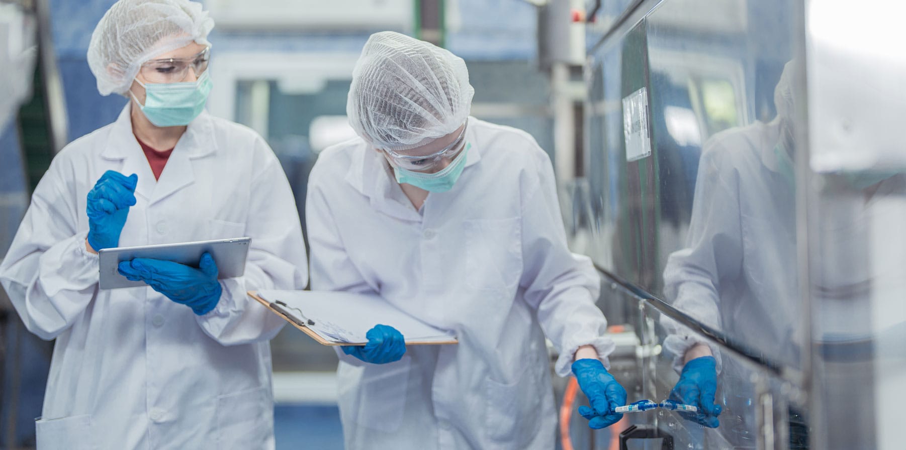 Female factory workers check machine systems in a clean room at an industrial factory